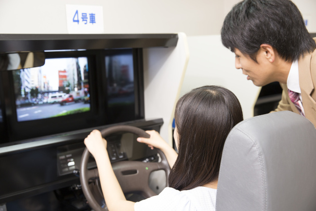 ドライブシュミレーターで練習をする女性と自動車教習所教官